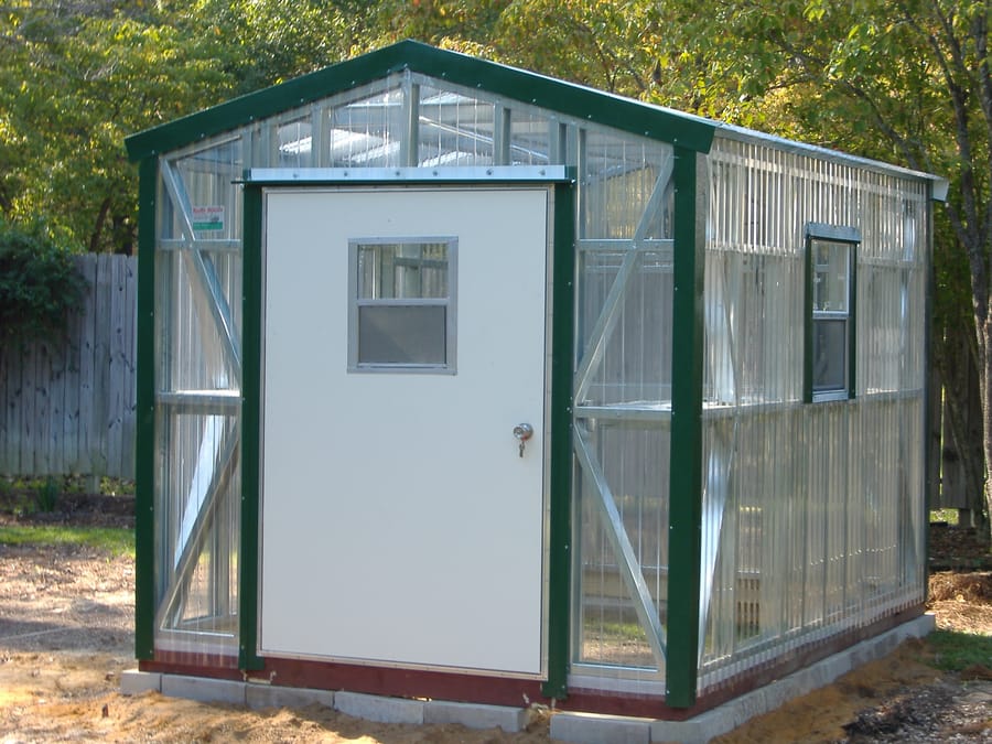 Greenhouse with clear polycarbonate panels, green trim, and mobile-home door